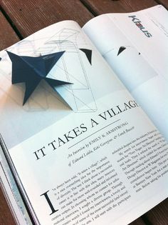 an open book with black origami stars on the page and title it takes a village