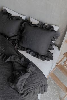 a bed with black ruffles and pillows on it next to a wooden chair