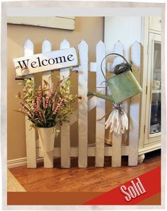 a white picket fence with some flowers and a watering can on it's side