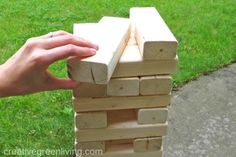 a person is building a tower made out of wood blocks on the sidewalk in front of some grass