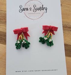 two red bows are attached to green and white flowery earrings on top of a card