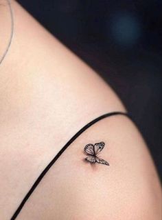 a small butterfly tattoo on the back of a woman's left shoulder, which is black and white