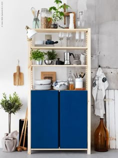 a blue cabinet sitting next to a white wall with plants on it and other kitchen utensils