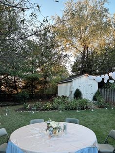 an outdoor table set up for a party with white balloons and blue cloths on it