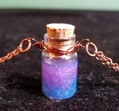 "Potion Bottle Necklace in shimmering purple and blue. This miniature corked glass bottle is filled with hardened resin and glitter, and wrapped in brown copper wire. Double stranded copper chain with copper lobster clasp closure is adjustable from 15.5\"-17.75\"." Potion Bottle Necklace Diy, Witch Potion Necklace, Blue Potion Bottle, Tiny Bottle Necklaces, Fairy Bottle Necklace, Bottle Necklace, Potion Bottle, Copper Chain, Copper Wire