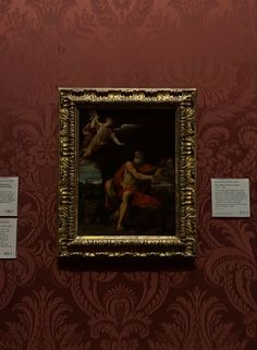 a painting on display in a room with red wallpaper