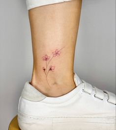 a small flower tattoo on the side of a woman's lower leg, with pink flowers