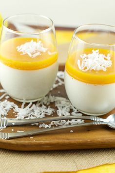 two glasses filled with dessert sitting on top of a wooden tray next to silverware