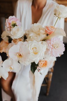 a bride holding a bouquet of white and pink flowers on her wedding day in a chair