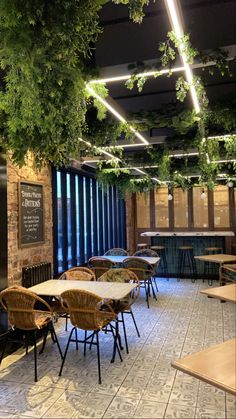 an empty restaurant with tables and chairs covered in green plants hanging from the ceiling above