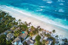 an aerial view of a beach with palm trees and blue water in the background,