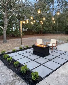 an outdoor fire pit with two chairs and lights hanging from the trees in the background