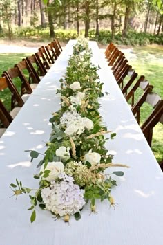 a long table with white flowers and greenery on it is set up for an outdoor dinner