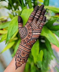 a woman's hand with henna tattoos on it and green leaves in the background