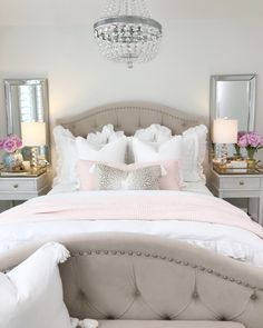 a white bed with pink pillows and some chandelier hanging from it's ceiling