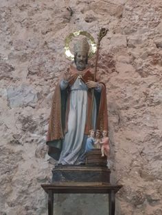 a statue of the virgin mary in front of a stone wall with a cross on it