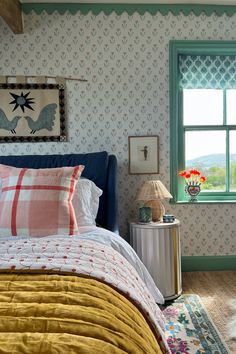 a bed sitting under a window next to a lamp on top of a table in front of a window