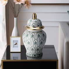 a white vase with gold trim sitting on a table next to a framed photograph and flowers