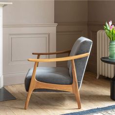 a grey chair sitting in front of a fireplace next to a vase with flowers on it