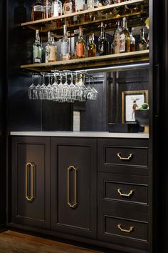 a bar with lots of bottles and glasses on the top shelf, along with wine glasses