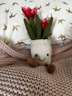 a small vase with flowers in it sitting on a bed next to a pillow and blanket