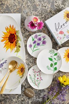 plates with flowers painted on them are sitting next to a box and spoons in front of it