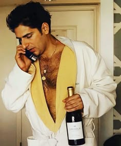 a man with no shirt talking on a cell phone and holding a bottle of wine