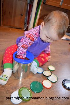 a toddler playing with some buttons on the floor in front of a cup and spoons