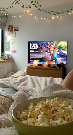 a person laying in bed with a bowl of popcorn and a television on the wall