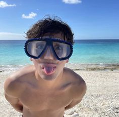 a shirtless man wearing goggles on the beach with his tongue hanging out and making a funny face