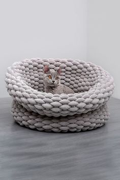 a cat is sitting in a basket made out of white yarn on top of a table