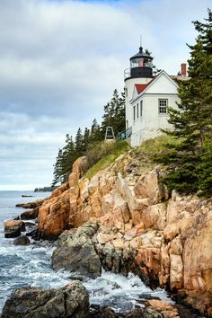 a lighthouse on top of a rocky cliff next to the ocean with trees around it