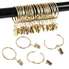 several pairs of rings and earrings hanging from a black rod with gold colored metal clips