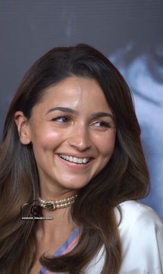 a woman with long brown hair wearing a white shirt and smiling in front of a movie poster