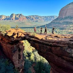 three people are standing on the edge of a cliff with mountains in the back ground