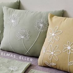 three pillows with embroidered flowers on them sitting on a couch next to two pillow cases