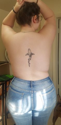 a woman with a dolphin tattoo on her back, standing in front of a mirror