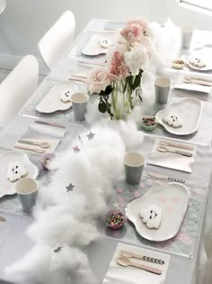 the table is set with white plates and silverware, pink flowers, and fluffy clouds