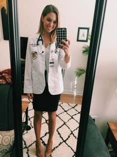 a woman taking a selfie in front of a mirror wearing a white lab coat