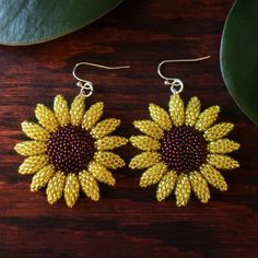 two yellow sunflowers are hanging from earrings on a wooden table next to a green leaf