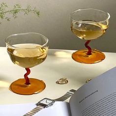 two glasses of wine sitting on top of a table with an open book next to them