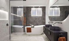 a large bathroom with two sinks and a bathtub in the center, along with an oval mirror on the wall