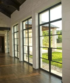 an empty room with wooden floors and large windows on both sides, looking out onto a grassy area