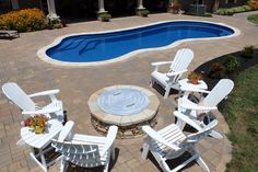 an empty pool with chairs around it and a fire pit in the middle surrounded by brick pavers