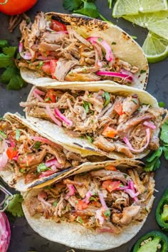 three shredded pork tacos with cilantro, red onion and lime wedges