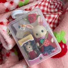 a couple of small toy animals in a plastic container on a pink blanket with red and white checkered pillows