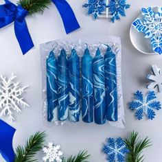 blue candles are in a box surrounded by snowflakes and christmas tree branches on a white surface