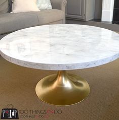 a white marble table with gold base in a living room area next to a couch