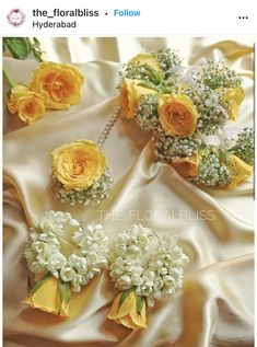 yellow roses and baby's breath flowers are arranged on a white satin fabric with green leaves