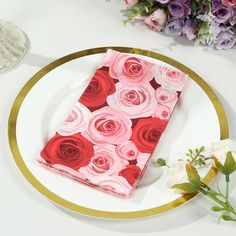 a white plate topped with a napkin covered in pink and red roses next to flowers